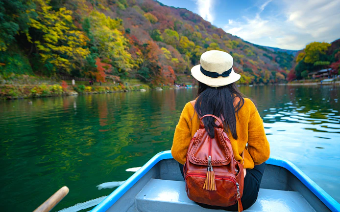 Person on boat on Hozugawa River, Kyoto, surrounded by autumn foliage.