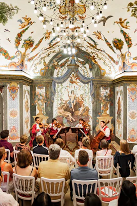 String quartet performing at Mozarthouse concert hall with ornate frescoes and audience seated.