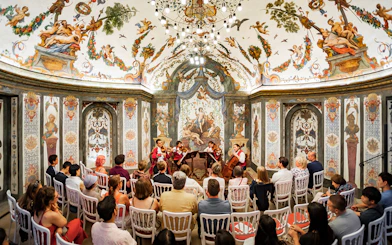 String quartet performing at Mozarthouse concert hall with ornate frescoes and audience seated.