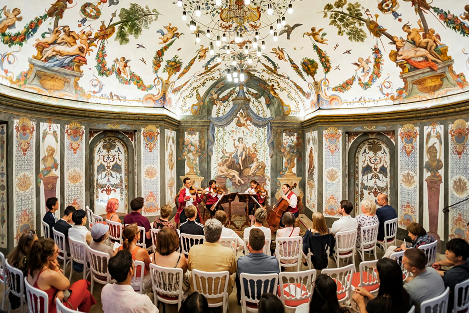 String quartet performing at Mozarthouse concert hall with ornate frescoes and audience seated.