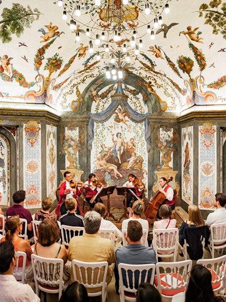 String quartet performing at Mozarthouse concert hall with ornate frescoes and audience seated.