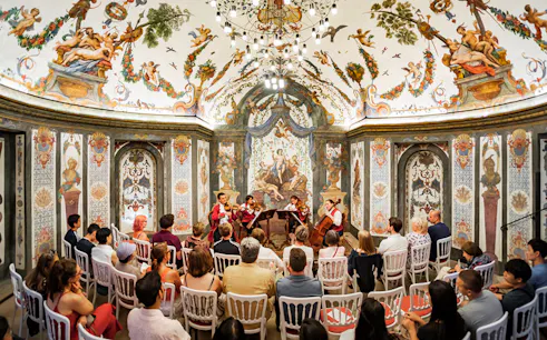 String quartet performing at Mozarthouse concert hall with ornate frescoes and audience seated.