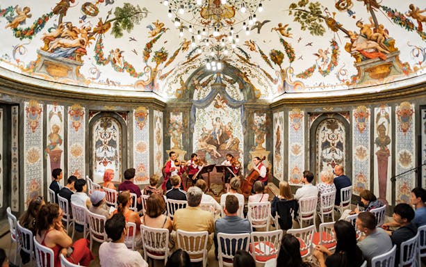 String quartet performing at Mozarthouse concert hall with ornate frescoes and audience seated.