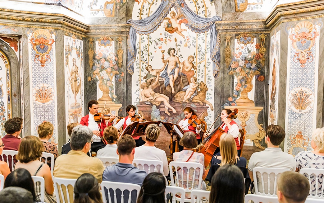 String quartet performing at Mozarthouse concert with ornate frescoes in the background.