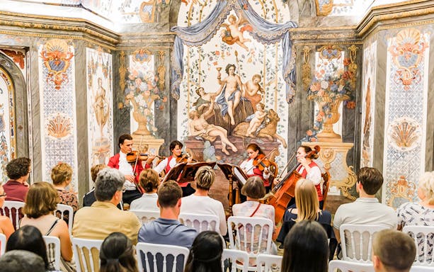 String quartet performing at Mozarthouse concert with ornate frescoes in the background.
