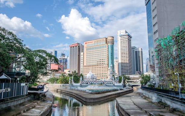 Kuala Lumpur cityscape with river, modern skyscrapers, and historic Sultan Abdul Samad Building.