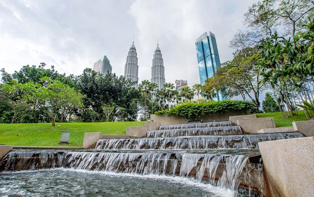 KLCC Park waterfall with Petronas Towers and KL Tower in Kuala Lumpur.