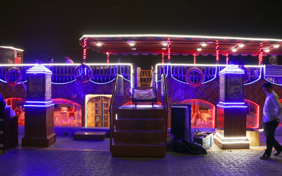 Dhow boat cruising Dubai Creek at night with live entertainment on deck.
