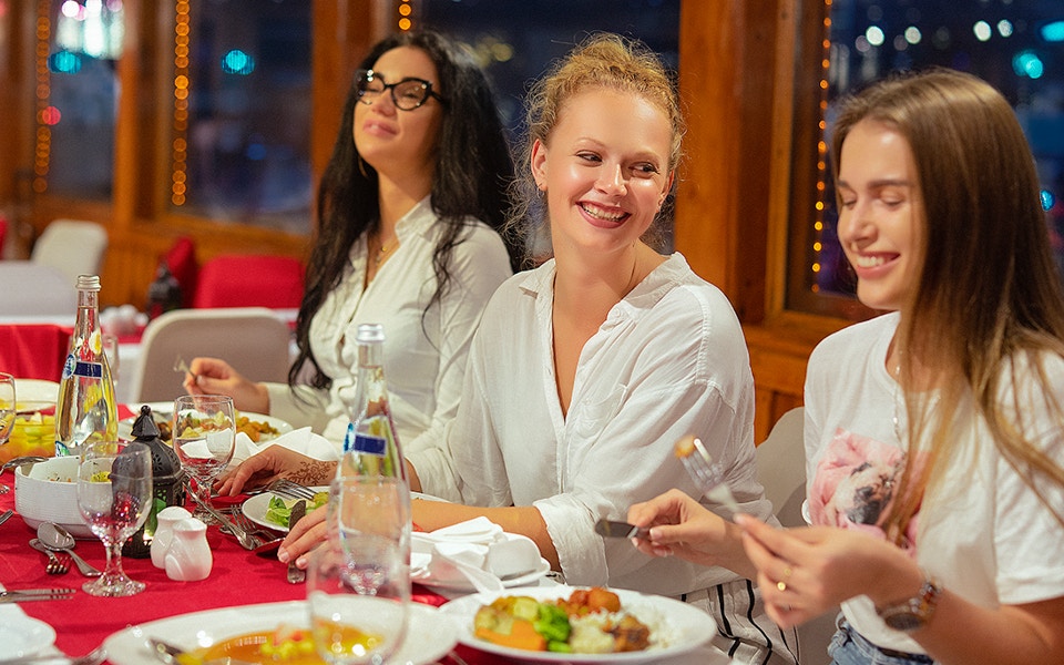 Dhow boat cruising Dubai Creek at night with live entertainment on deck.