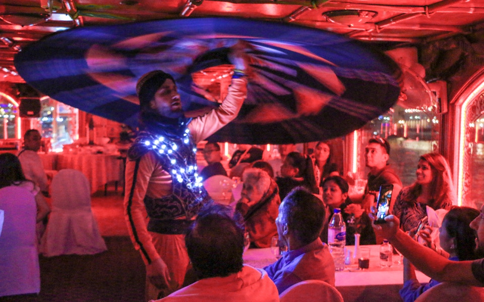 Dhow boat cruising Dubai Creek at sunset with live entertainment on deck.