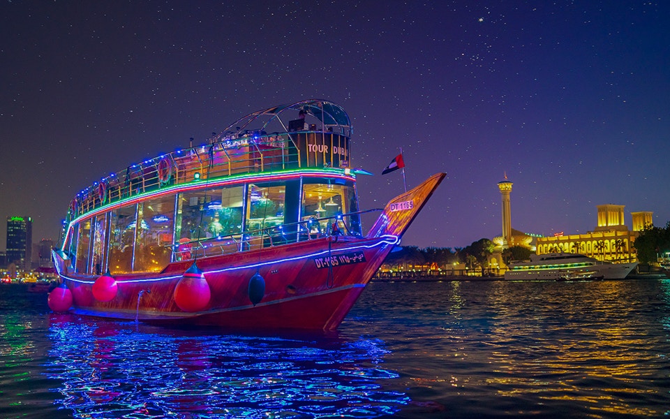 Dhow sailing on Dubai Creek with guests enjoying dinner and live entertainment.