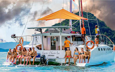 Group enjoying a sunset cruise on a catamaran in Langkawi, with lush hills in the background.