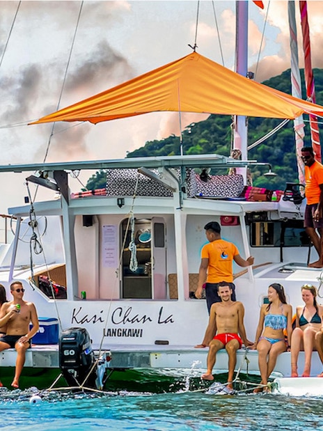 Group enjoying a sunset cruise on a catamaran in Langkawi, with lush hills in the background.