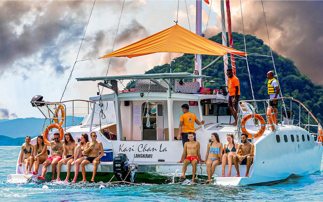 Group enjoying a sunset cruise on a catamaran in Langkawi, with lush hills in the background.