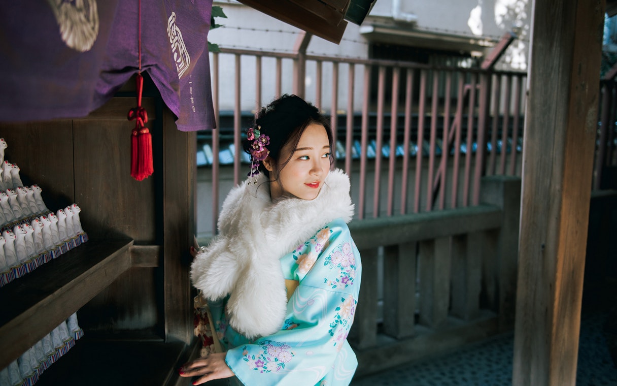 Woman in traditional kimono at a Tokyo shrine, surrounded by small fox statues.