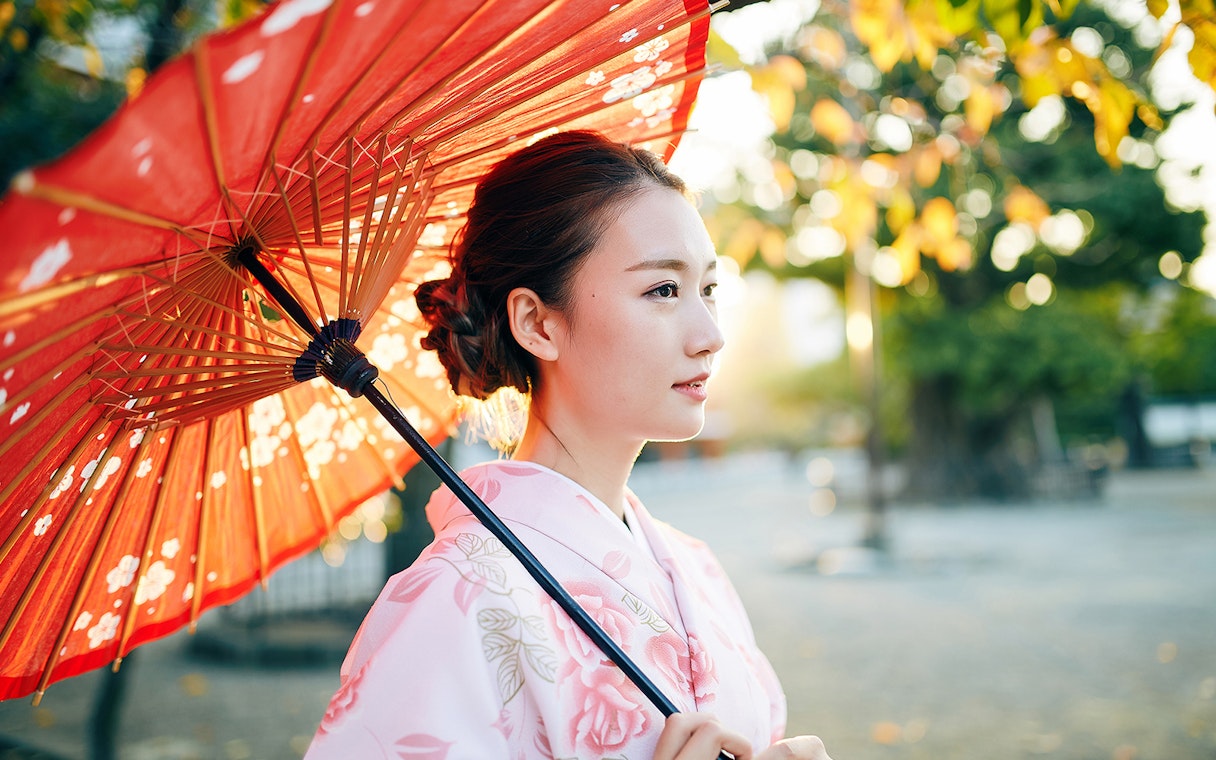 Person in kimono holding a red parasol in a Tokyo garden.