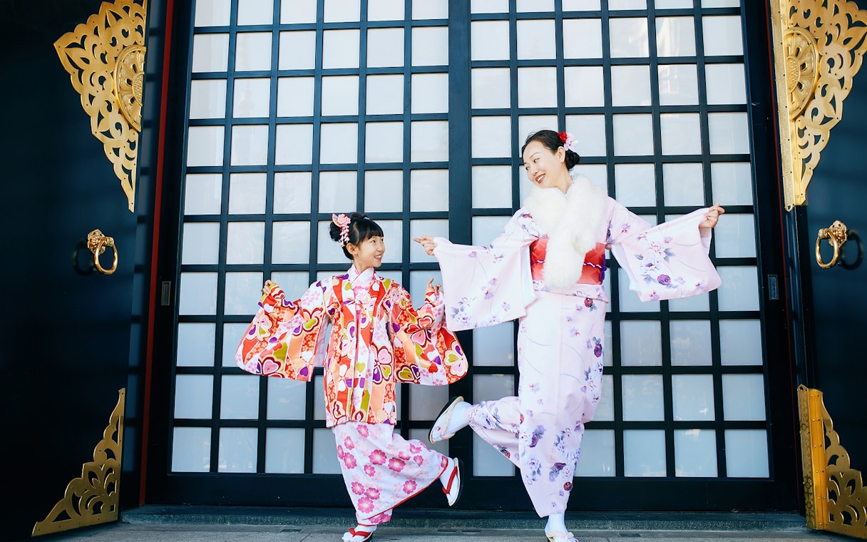 Two people in colorful kimonos posing in front of a traditional Japanese gate in Tokyo.