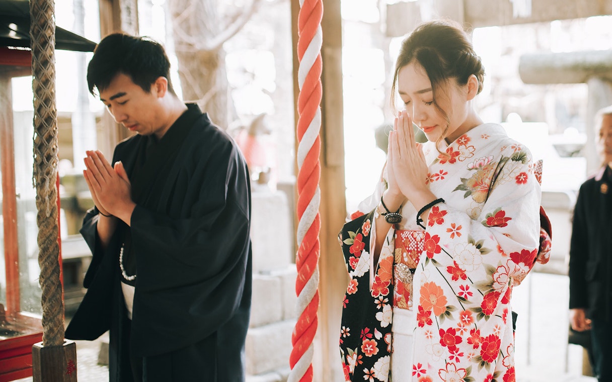 People in traditional kimonos praying at a Tokyo shrine.