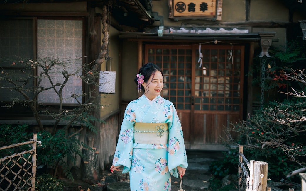 Woman in a floral kimono standing outside a traditional Japanese house in Tokyo.