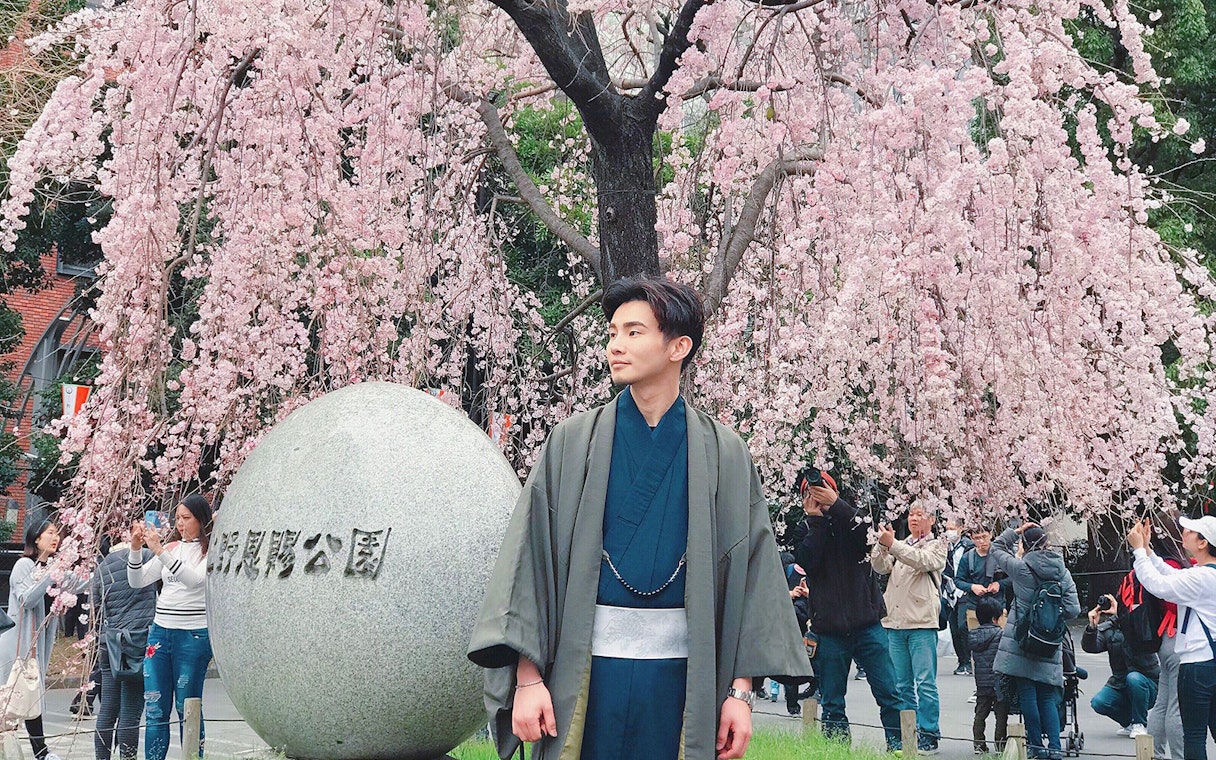 Man in kimono under cherry blossoms in Tokyo park.