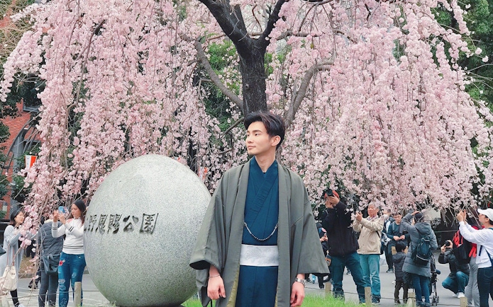 Man in kimono under cherry blossoms in Tokyo park.