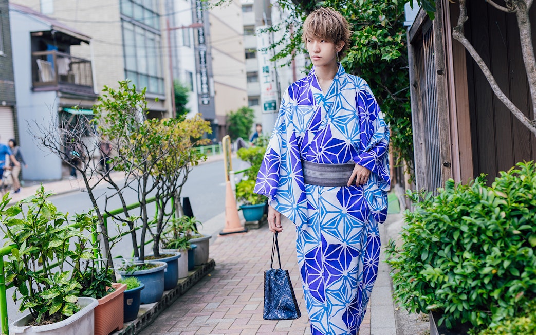 Person in blue kimono walking on a Tokyo street, holding a bag.