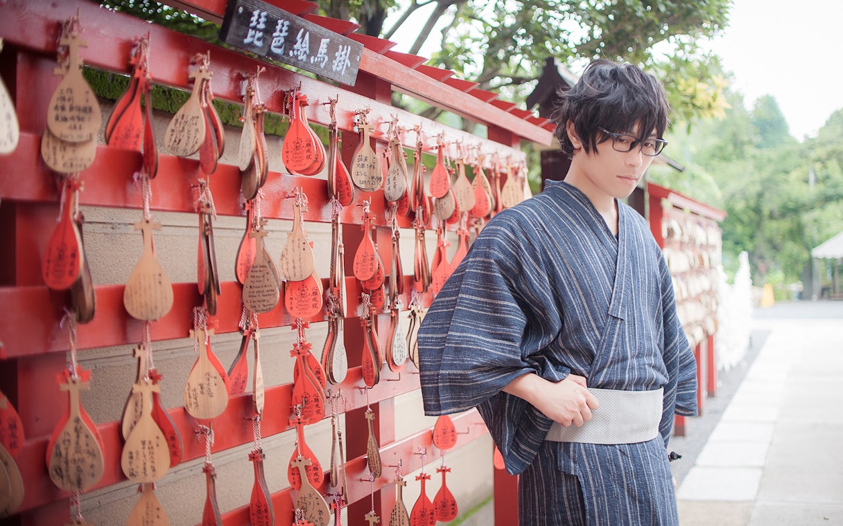 Person in kimono standing by ema prayer plaques in Tokyo.