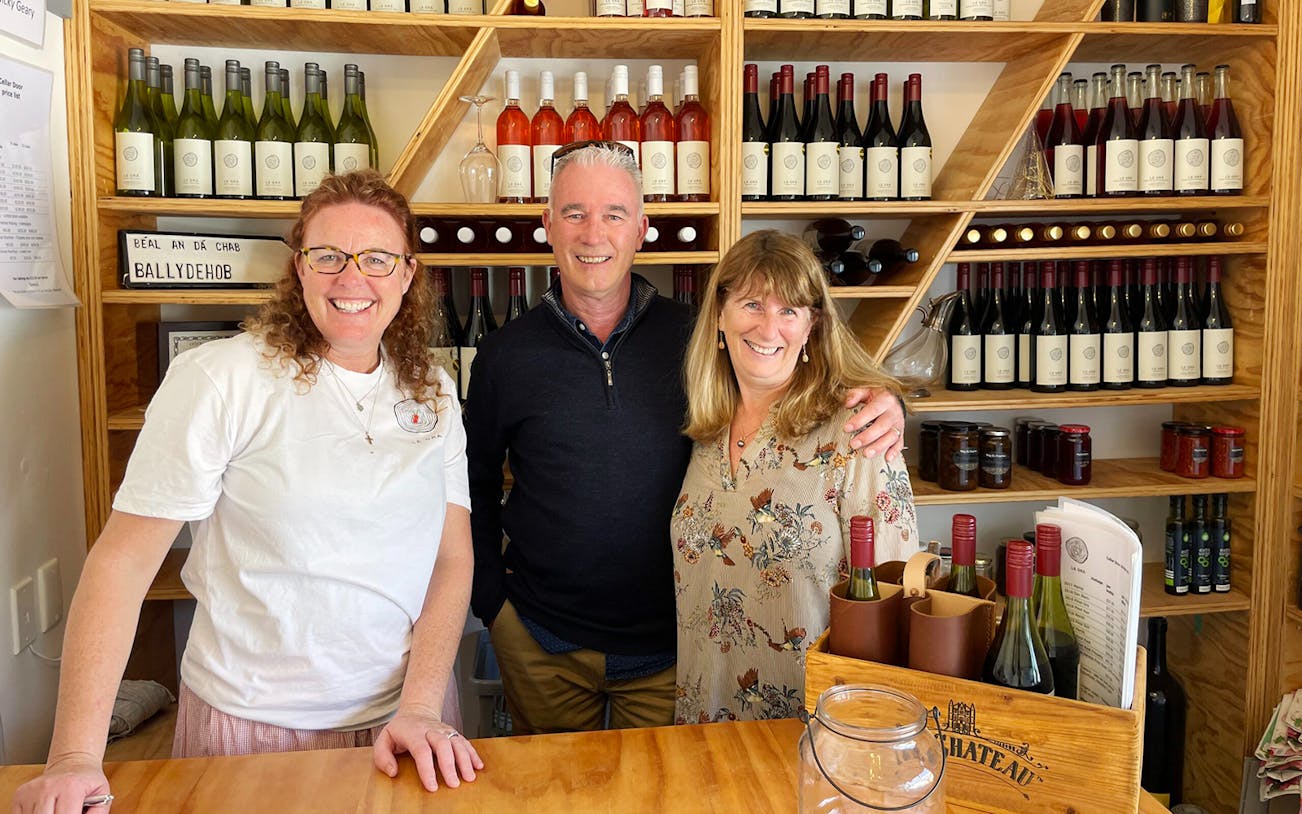 Three people smiling in a Martinborough winery, surrounded by wine bottles.