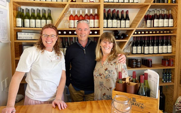 Three people smiling in a Martinborough winery, surrounded by wine bottles.