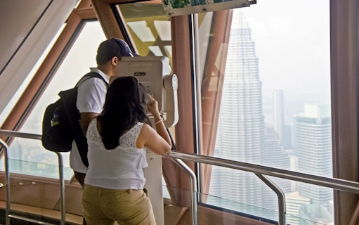 Visitors using binoculars at KL Tower's Observation Deck with view of Petronas Towers, Malaysia.