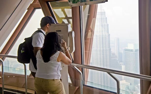 Visitors using binoculars at KL Tower's Observation Deck with view of Petronas Towers, Malaysia.