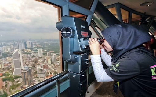Tourist using binoculars on KL Tower observation deck overlooking Kuala Lumpur.