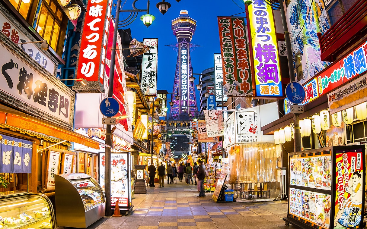 Bustling Osaka street with neon signs and Tsutenkaku Tower, near Redhorse Osaka Wheel.