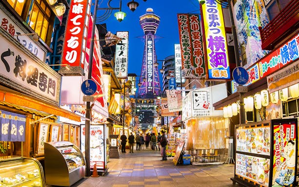 Bustling Osaka street with neon signs and Tsutenkaku Tower, near Redhorse Osaka Wheel.
