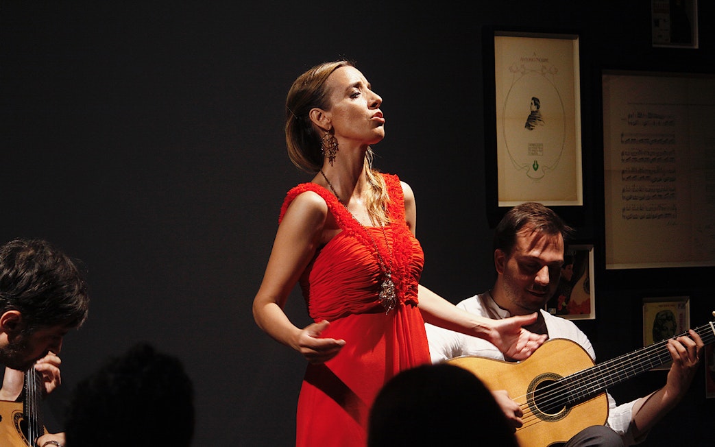 Singer performing Fado music with guitarists at Ideal Clube concert.