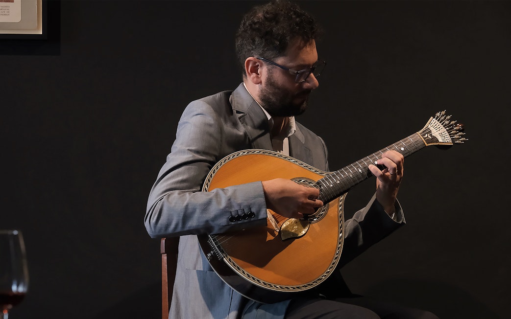 Musician playing Portuguese guitar at Ideal Clube Fado concert.