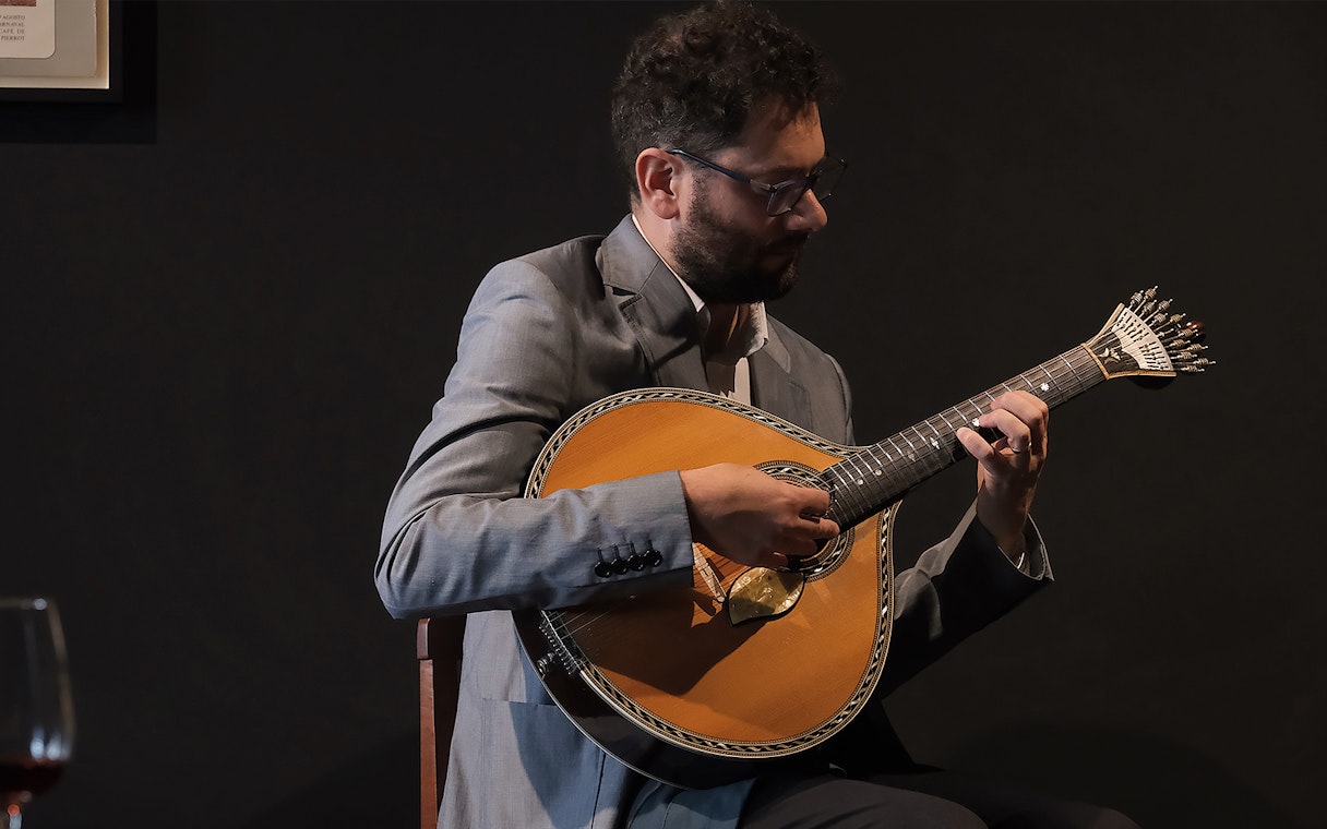 Musician playing Portuguese guitar at Ideal Clube Fado concert.