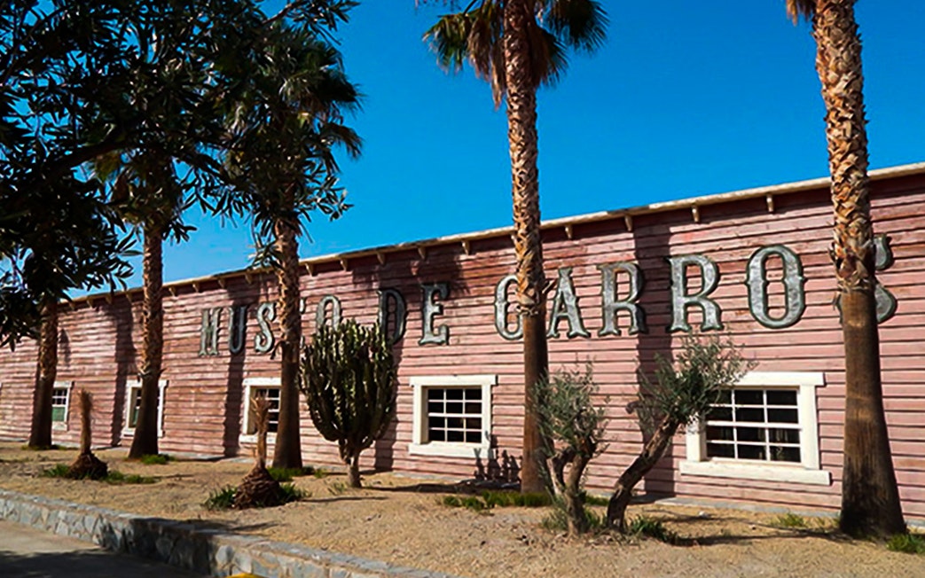 Exterior of Museo de Carros at Oasys MiniHollywood, Almería, with palm trees and cacti.