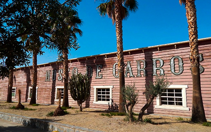Exterior of Museo de Carros at Oasys MiniHollywood, Almería, with palm trees and cacti.