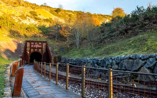 Entrance to El Soplao Cave in Cantabria, Spain, surrounded by lush hillside.