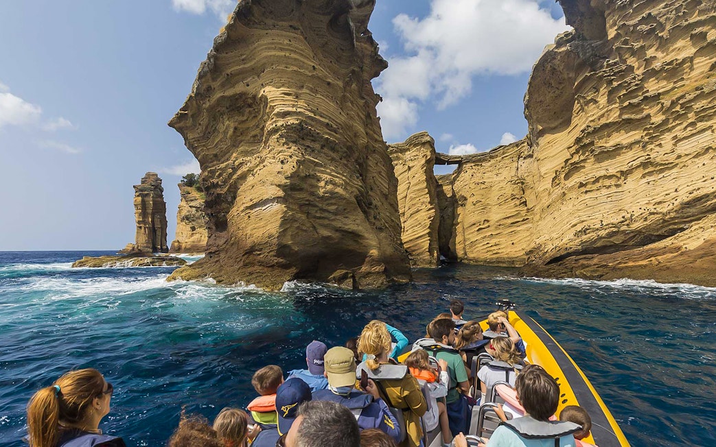 Boat tour approaching rock formations at Azores Island during whale watching excursion.