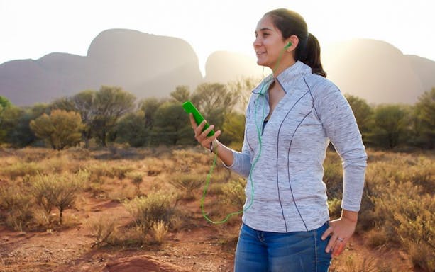 Person using audio guide at Uluru with rock formations in the background.