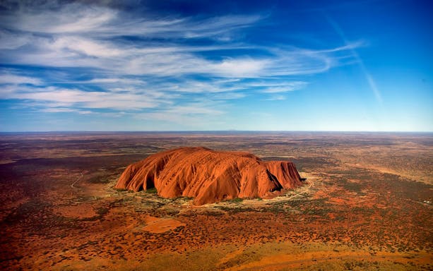 Aerial view of Uluru in Australia with surrounding desert landscape.