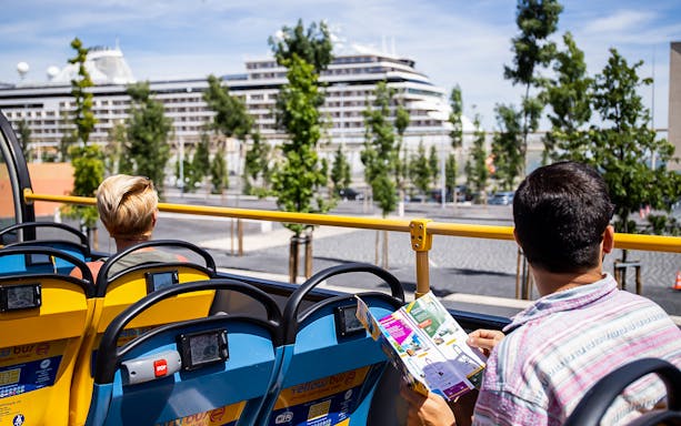 Lisbon hop-on hop-off bus with passengers viewing a map, cruise ship in background.