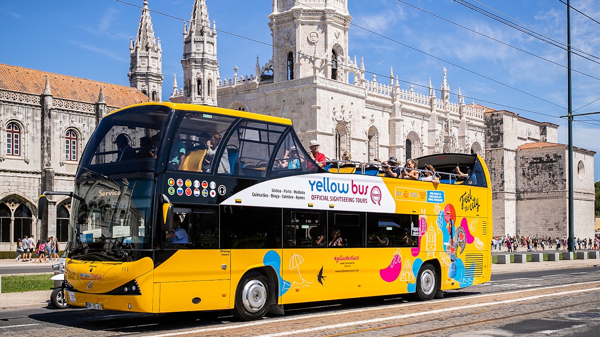 Yellow bus on Lisbon hop-on hop-off tour passing Jerónimos Monastery.