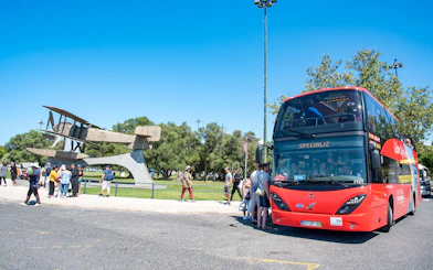 Lisbon hop-on hop-off bus near airplane sculpture with tourists boarding.