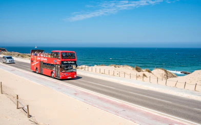 Lisbon sightseeing bus on coastal road with ocean view.