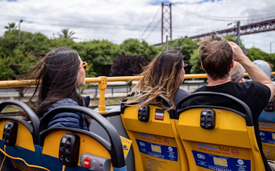 Tourists on Lisbon hop-on hop-off bus with view of 25 de Abril Bridge.