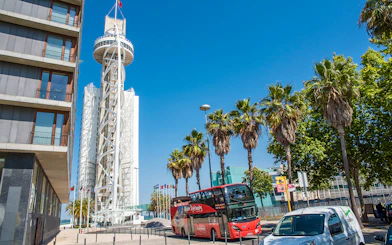Lisbon sightseeing bus near Vasco da Gama Tower with palm trees and clear sky.
