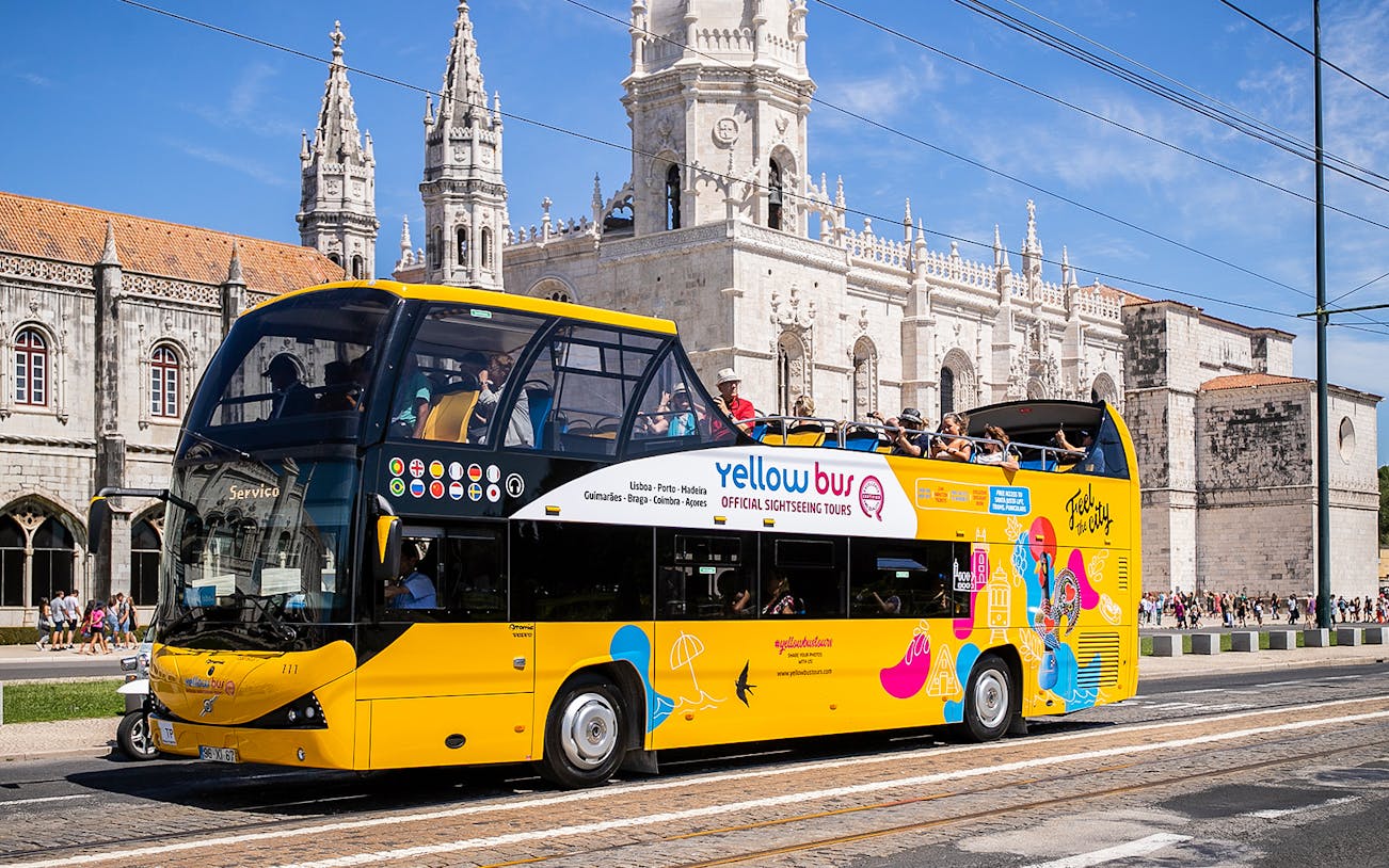 Open-top yellow tour bus in front of Jerónimos Monastery, Lisbon.